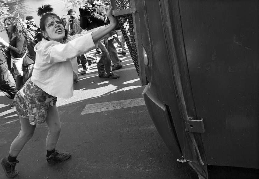 Una manifestante empuja un vehículo de la Policía durante los incidentes a las afueras del edificio del Congreso Nacional chileno, en Valparaíso, mientras el presidente Sebastián Piñera presentaba la tercera cuenta pública de su gobierno 