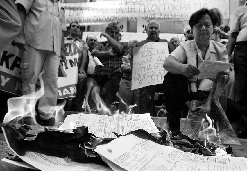Activistas del sindicato griego PAME, afiliado al Partido Comunista (KKE), queman sus documentos fiscales para el pago de sobreimpuesto extraordinario que grava el patrimonio inmobiliario, durante una manifestacion convocada a las puertas de la delegacion de Hacienda, el jueves en Atenas. 