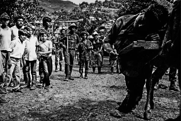 Niños observan los cuerpos de integrantes de los Contras muertos en combate al intentar, en la víspera del 15 de noviembre de 1985, tomar Santo Domingo, en el departamento de Chontales, en Nicaragua, al ser llevados al poblado por miembros del Batallón de Lucha Irregular Farabundo Martí del Ejército Popular Sandinista.