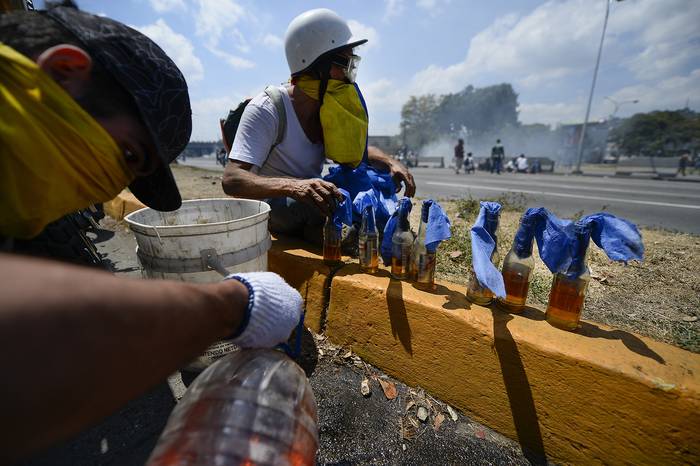 Manifestantes de la oposición preparan cócteles molotov durante los enfrentamientos con soldados leales al presidente venezolano Nicolas Maduro, en los alrededores de la base militar de La Carlota, en Caracas. · Foto:  Matias Delacroix / AFP)