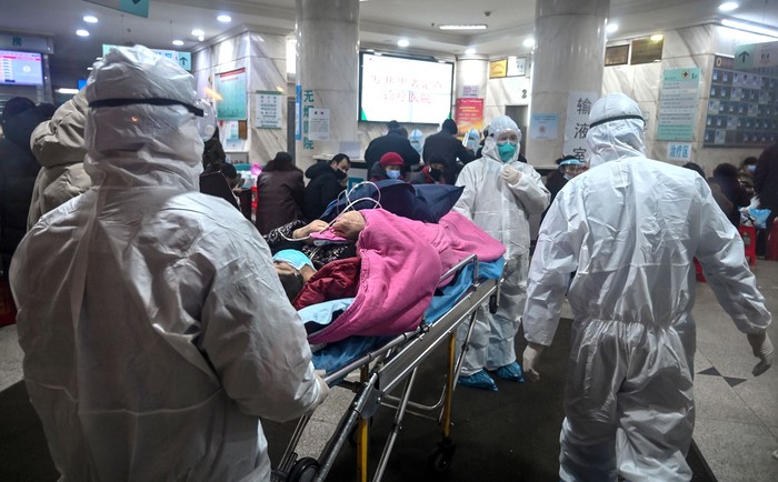 Personal médico con ropa aislante para protegerse contra un coronavirus atiende a un paciente en el hospital de la Cruz Roja de Wuhan. · Foto: Héctor Retamal / AFP