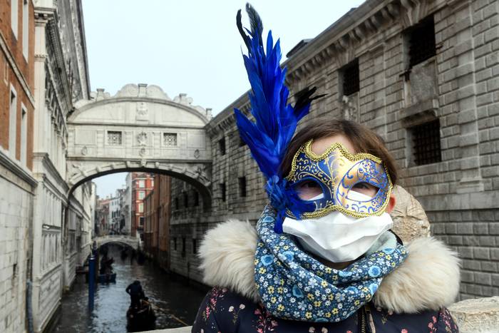 Un turista con una máscara protectora y una máscara de carnaval, el 24 de febrero de 2020, durante el período habitual de las festividades de Carnaval que se cancelaron los últimos dos días debido a un brote del nuevo coronavirus. · Foto: Andrea Pattaro, AFP