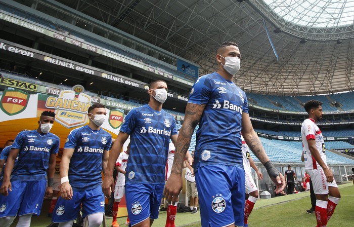 Los jugadores de Gremio ingresan al campo con máscaras protectoras para evitar la propagación del nuevo Coronavirus, antes del partido contra Sao Luiz, en el estadio Arena do Gremio, a puertas cerradas, en Porto Alegre, Brasil, el 15 de marzo de 2020. Richard Pato / AFP