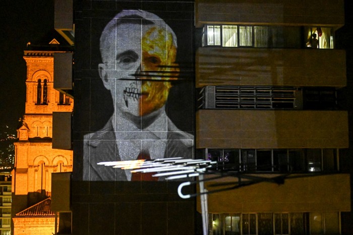 Un hombre mira por una ventana mientras una imagen del expresidente colombiano (2002-2010) Álvaro Uribe es proyectada en el muro de su edificio, como parte de una nueva forma de protestar en Medellín. · Foto: Joaquín Sarmiento, AFP