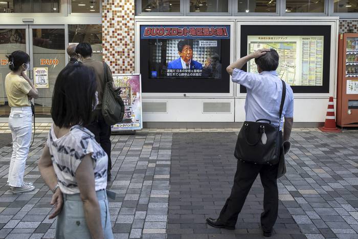 Gente en Tokio frente a un televisor que transmite las noticias sobre el ataque contra el ex primer ministro japonés Shinzo Abe más temprano ese día, a lo largo de una calle de Tokio el 8 de julio de 2022. · Foto: Charly Triballeau, AFP