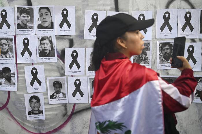 Manifestante y pared cubierta con imágenes de las víctimas durante una protesta en contra del gobierno de Dina Boluarte, el 31 de enero, en Lima. · Foto: Ernesto Benavides, AFP