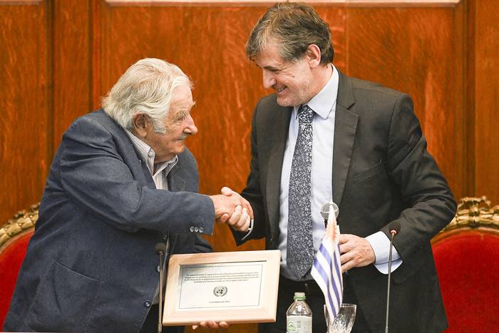 El expresidente de Uruguay José Mujica recibe un reconocimiento de manos del jefe de reincorporación de la Misión de Verificación de las Naciones Unidas en Colombia, Alessandro Preti, por su contribución al proceso de paz en Colombia, este jueves, en el paraninfo de la Universidad de la República. · Foto: Pablo Porciúncula, AFP.