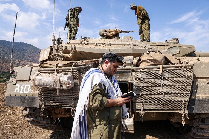 Un soldado israelí reza frente a un tanque Merkava en las afueras de la ciudad norteña de Kiryat Shmona, el 8 de octubre cerca de la frontera con el Líbano. Foto: Jalaa Marey, AFP