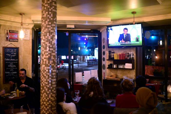Clientes de un bar siguen el discurso televisado en el que el presidente francés, Emmanuel Macron, anuncia el regreso al confinamiento en todo el país · Foto: Martin Bureau, AFP