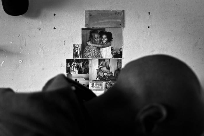 Damián en su habitación, leyendo. Atrás, la foto principal muestra a su madre y a su hija. · Foto: Ricardo Antúnez