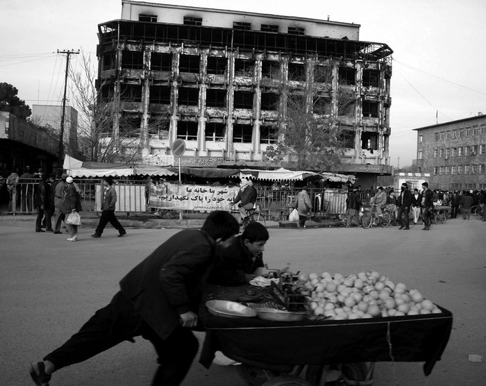 Afganos pasan delante de un centro comercial que fue el campo de batalla entre los talibanes y las fuerzas del gobierno el 18, en Kabul, día en que el presidente Hamid Karzai tomó el juramento a 14 miembros de su nuevo gabinete de gobierno.  · Foto: Efe, S Sabawoon