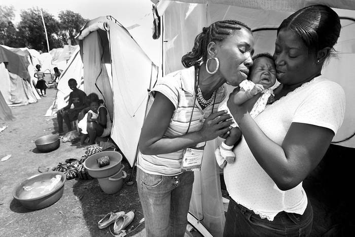Elvire Constant, directora de la fundación local OFAPAA, besa a un bebé y da consejos de tratamiento médico y de nutrición a su madre, en un área del campo Delmas 33 IDP, en Puerto Príncipe.  · Foto: Efe, Sophia Paris, ONU, Minustah