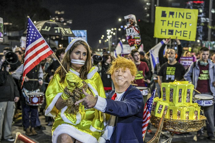 Una mujer vestida como rehén israelí sentada en el regazo de un hombre vestido como el presidente electo de Estados Unidos, Donald Trump,  durante una protesta antigubernamental que pide medidas para asegurar la liberación de los rehenes israelíes cautivos, el 21 de diciembre, en Tel Aviv. · Foto: Jack Guez, AFP