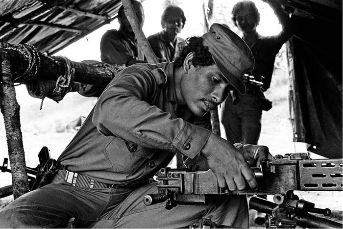 Un miembro del Ejército Popular Sandinista limpia una metralleta de pie en un puesto militar del poblado de indígenas misquitos Haulover, en la costa atlántica de Nicaragua, en 1984. · Foto: Daniel Caselli