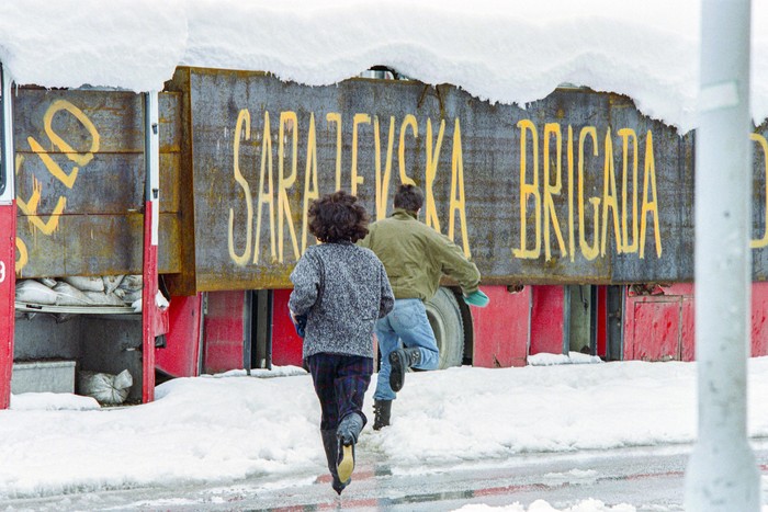 Una pareja corre a refugiarse de los francotiradores detrás de un autobús con la leyenda "Brigada Sarajevo", el 28 de marzo de 1993 en Sarajevo, durante la guerra de Bosnia. · Foto: Vincent Amalvy, AFP