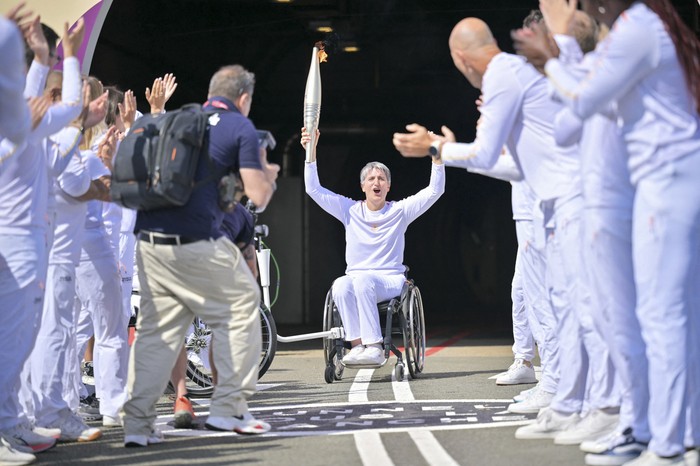 La exesgrimista francesa en silla de ruedas Emmanuelle Assmann sostiene la antorcha paralímpica después de la llegada de la llama de los Juegos Paralímpicos de París 2024, a la entrada del Túnel del Canal en Coquelles, norte de Francia, el 25 de agosto de 2024. · Foto: Lou Benoist, AFP