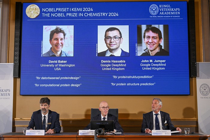 Heiner Linke, presidente del Comité del Premio Nobel de Química; Hans Ellegren, secretario general de la Real Academia Sueca de Ciencias, y Johan Aqvist, el miembro del Comité del Premio Nobel de Química, anuncian los galardonados con el Premio Nobel de Química 2024 (en la pantalla, de izquierda a derecha): David Baker, Demis Hassabis y John M Jumper, el 9 de octubre, en la Real Academia Sueca de Ciencias, en Estocolmo. · Foto: Jonathan Nackstrand, AFP