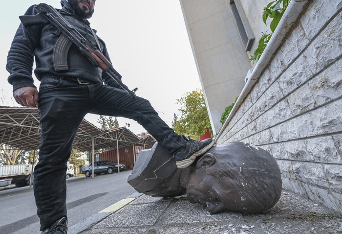 Un combatiente antigubernamental pisa la cabeza de una estatua del difunto presidente sirio Hafez al Assad, el 9 de diciembre de 2024, en Damasco. · Foto: Louai Beshara, AFP