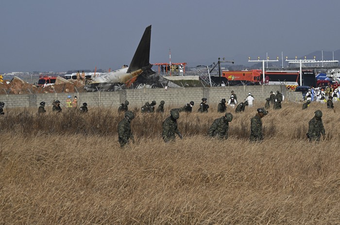 Soldados surcoreanos buscan pasajeros desaparecidos cerca de los restos de un avión Boeing 737-800 de Jeju Air después de que se estrellara y estallara en llamas en el Aeropuerto Internacional de Muan, en la provincia de Jeolla del Sur, a unos 288 kilómetros al suroeste de Seúl. · Foto: Jung Yeon-je, AFP