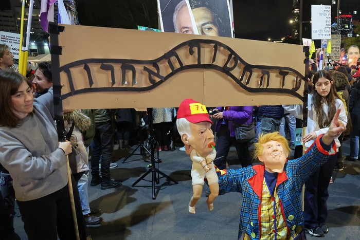 Un manifestante con una máscara de Donald Trump sostiene un muñeco con una máscara del primer ministro israelí Benjamin Netanyahu mientras posa frente a una réplica del infame letrero en la entrada de Auschwitz, el campo de concentración nazi, durante una protesta que pide la liberación de los rehenes cautivos en Gaza desde el 7 de octubre. · Foto: Jack Guez, AFP