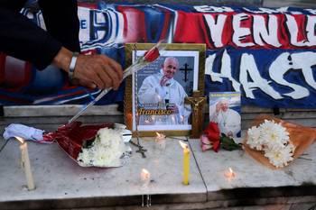 Un hombre coloca flores junto a un retrato del difunto papa Francisco en un altar improvisado frente a la entrada de la Catedral de Buenos Aires, el 21 de abril. · Foto: Luis Robayo, AFP