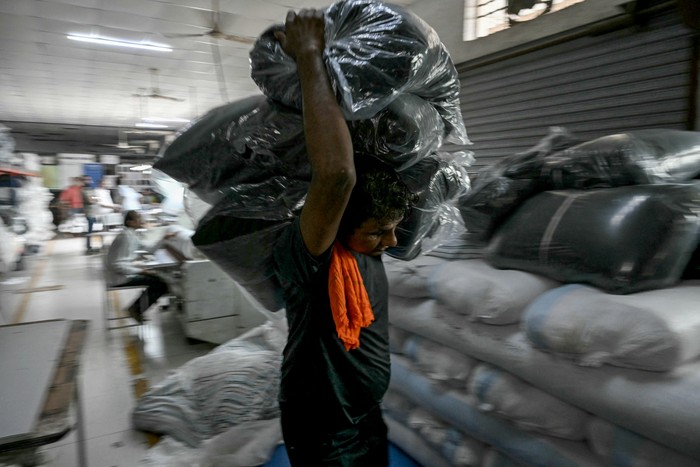 Un trabajador transporta fardos de tela para confección en la unidad de fabricación de prendas de vestir de Bhiwandi, en el distrito de Thane, estado indio de Maharashtra, el 30 de julio. · Foto: Indranil Mukherjee, AFP