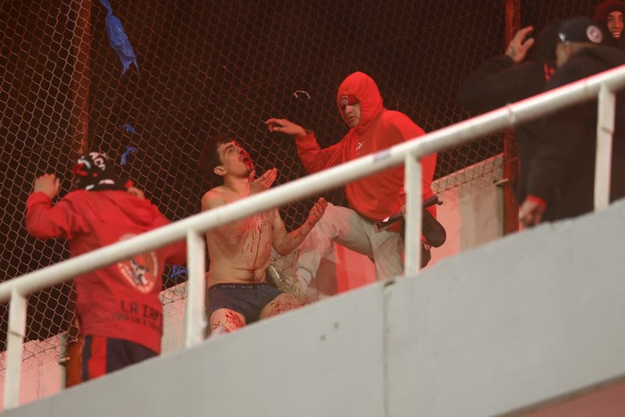 Un hincha de la Universidad de Chile sangra al ser golpeado por hinchas de Independiente, durante la interrupción del partido de vuelta, el 20 de agosto, en el estadio Libertadores de América, en Avellaneda, Buenos Aires. · Foto: Alejandro Pagni, AFP