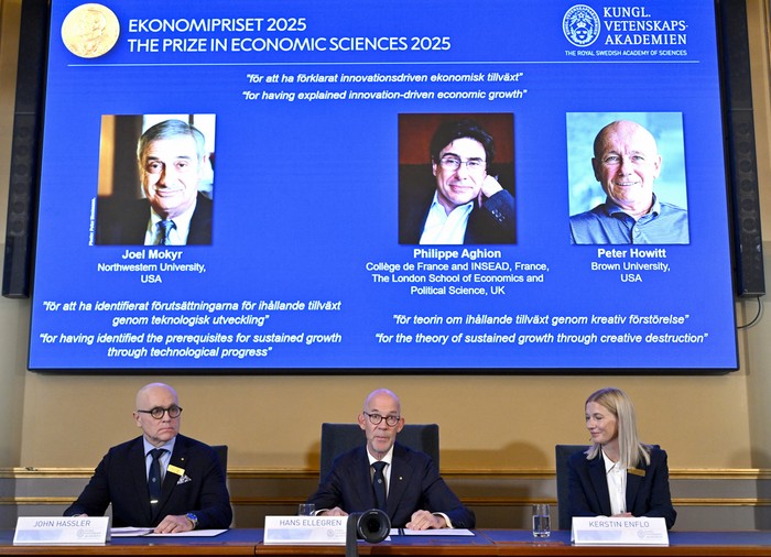 John Hassler, presidente del Comité del Premio en Ciencias Económicas en memoria de Alfred Nobel, el secretario general de la Real Academia Sueca de Ciencias, Hans Ellegren, y Kerstin Enflo, miembro del Comité del Premio en Ciencias Económicas, ante una pantalla que muestra los retratos de los ganadores del premio de 2025. · Foto: Anders Wiklund, Agencia TT, AFP