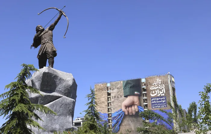 Una valla publicitaria en la fachada de un edificio que representa el estrecho de Ormuz con la leyenda en persa "Siempre en manos de Irán”, al frente escultura de Arash el Arquero, una figura legendaria de la mitología persa, en la plaza Vanak de Teherán. · Foto: Atta Kenare, AFP