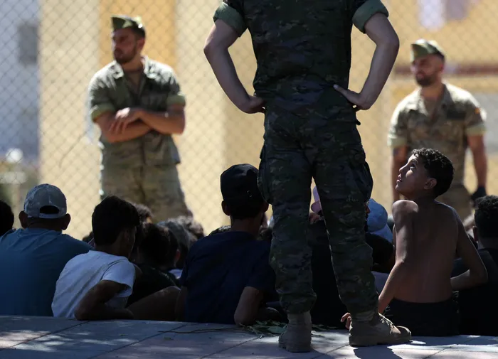 Migrantes y miembros del ejército español cerca del puesto fronterizo antes de ser escoltados de regreso a Marruecos, en el enclave español de Ceuta, el 2 de agosto. · Foto: Henry Nicholls, AFP