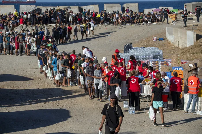Voluntarios de la Cruz Roja distribuyen alimentos a los migrantes que siguen viviendo en las calles, en la playa del Trampolín, en Ceuta, el 22 de agosto de 2026. · Foto: Antonio Sempere, AFP