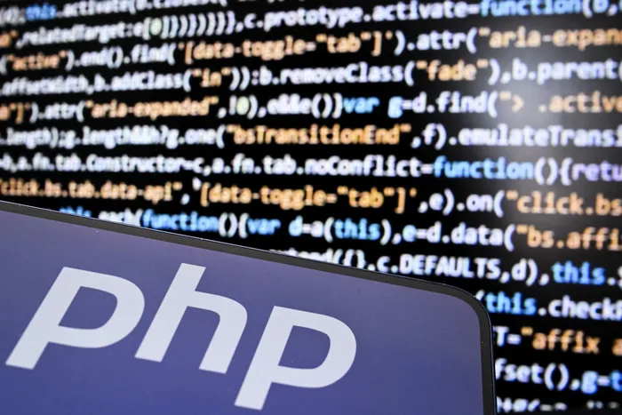 El logotipo PHP (preprocesador de hipertexto) en la pantalla de un teléfono inteligente y un código de computadora. · Foto: Kirill Kudryavstsev, AFP