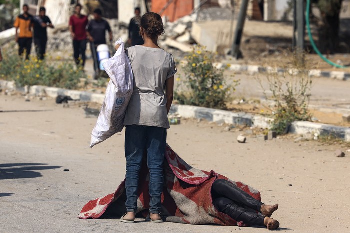 Una niña palestina junto al cuerpo de una persona que murió mientras buscaba comida en un punto de distribución gestionado por la Fundación Humanitaria de Gaza, el 4 de agosto, en la carretera de Saladino, en Nusseirat, en el centro de la Franja de Gaza. · Foto: AFP