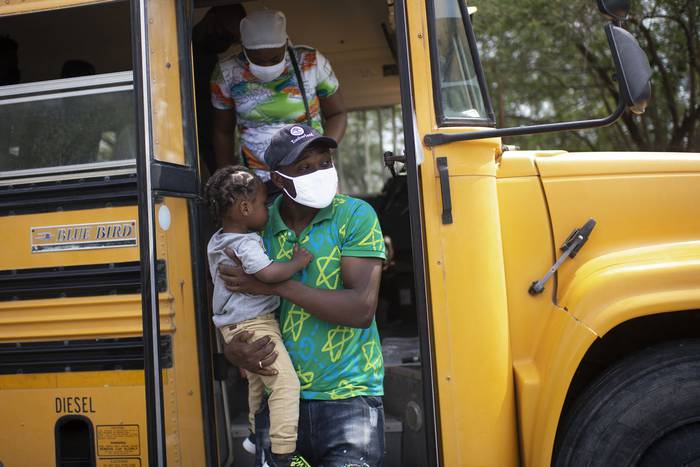 El migrante haitiano Jean Philippe Jocelin carga a su hijo seguido de su esposa Berline para dirigirse a un puerto de entrada de los Estados Unidos e iniciar el trámite legal en Reynosa, estado de Tamaulipas, México. · Foto: Pedro Pardo, AFP