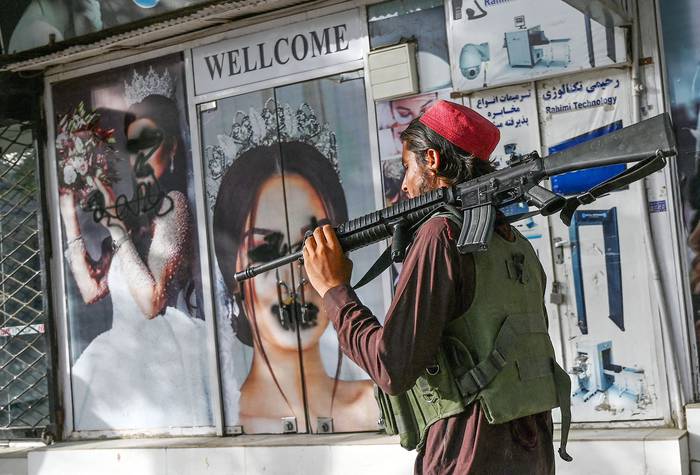 Un combatiente talibán pasa frente a un salón de belleza con fotos publicitarias desfiguradas con pintura en aerosol, ayer, en Shar-e-Naw, Kabul. · Foto: Wakil Kohsar, AFP
