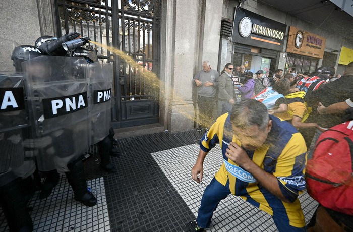 Un policía lanza gas pimienta contra un hincha de Rosario Central durante una protesta de jubilados que recibió apoyo de hinchas de fútbol, ​​contra el gobierno del presidente Javier Milei, el 12 de marzo, en Buenos Aires. · Foto: Luis Robayo, AFP