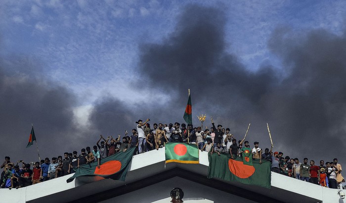 Manifestantes antigubernamentales exhiben la bandera nacional de Bangladesh mientras asaltan el palacio de la primera ministra Sheikh Hasina, el 5 de agosto, en Dhaka. · Foto: KM Asad, AFP