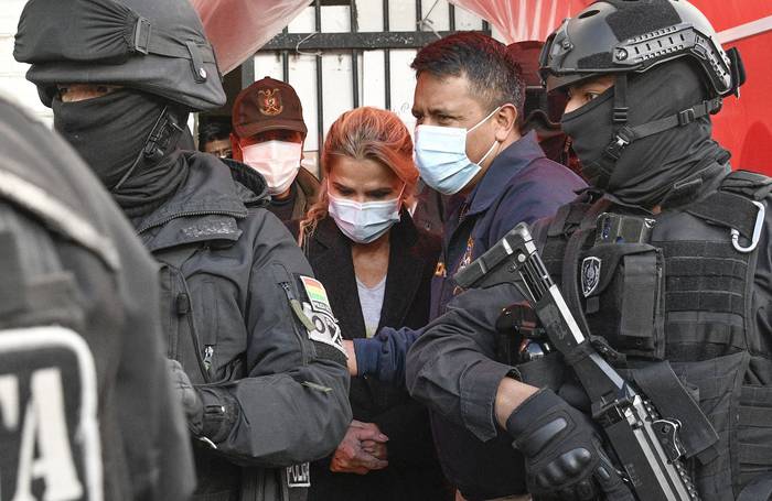 La ex presidenta interina de Bolivia Jeanine Añez es escoltada, luego de ser arrestada, por miembros de la Fuerza Especial contra el Crimen, el 13 de marzo de 2021, en La Paz. · Foto: Aizar Raldes, AFP