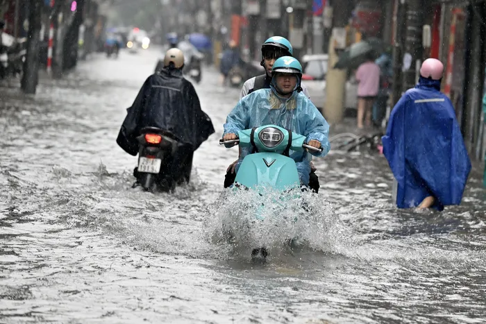 Un conductor de un servicio de transporte compartido traslada a un pasajero en un escúter eléctrico por una calle inundada de Hanói el 17 de septiembre de 2026. (Foto de Nhac NGUYEN / AFP)