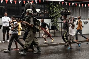 Un miembro del grupo armado M23 camina junto a residentes por una calle del barrio de Keshero, el 27 de enero, en Goma. · Foto: AFP