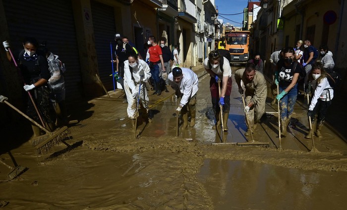 Voluntarios limpian agua fangosa tras las devastadoras inundaciones en Paiporta, Valencia. · Foto: José Jordan, AFP