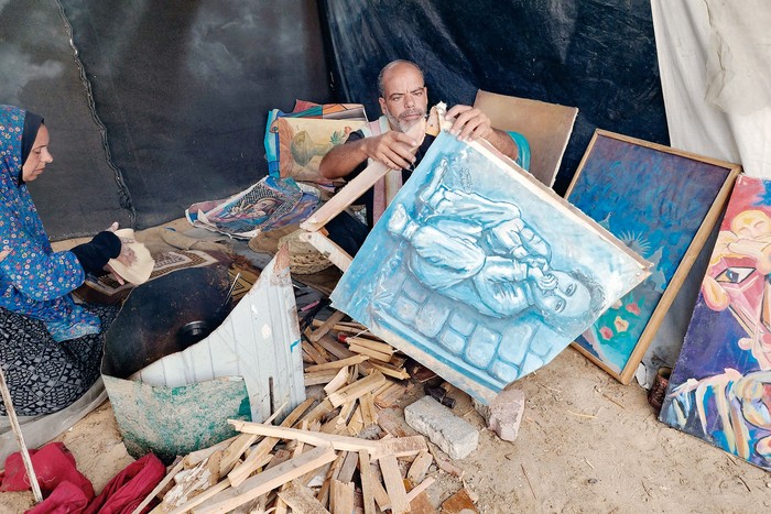 El pintor palestino Taha Abu Ghali desmantela sus obras para encender una fogata y poder cocinar para sus hijos en la región de al-Mawasi, en Khan Yunis, al sur de la Franja de Gaza, el 17 de agosto. · Foto: Hani Alshaer / Anadolu / AFP