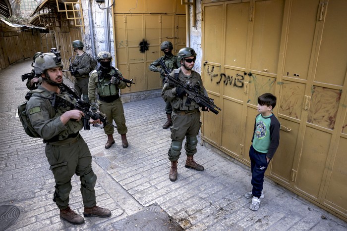 Soldados del ejército israelí hacen guardia mientras colonos judíos israelíes recorren el antiguo mercado de la ciudad de Hebrón, en la Cisjordania ocupada, el 28 de diciembre de 2024. · Foto: Hazem Bader, AFP