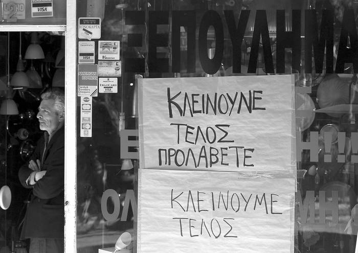 El propietario de una tienda espera junto al escaparate en el que ha colocado un anuncio de liquidación de la mercadería por cierre,
en el distrito comercial del centro de Atenas, el jueves 21 de abril de 2011.  · Foto: Efe, Orestis Panagiotou