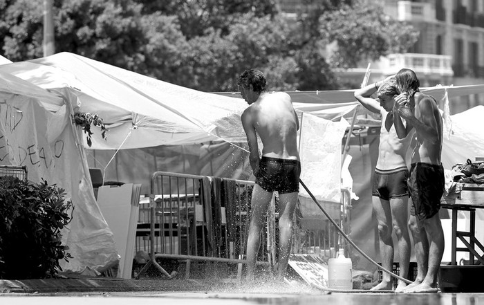 Jóvenes del movimiento de los "indignados" que permanecen acampados en la Plaza Catuluña, se asean utilizando una manguera a primera hora de la mañana. · Foto: Efe, Alberto Estévez