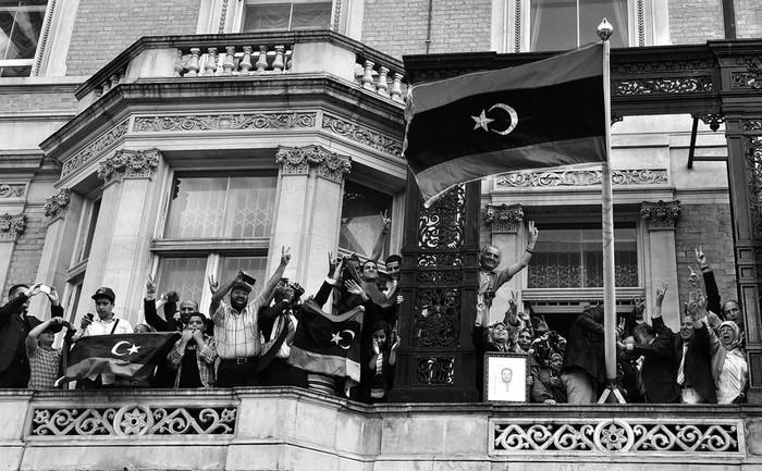 Miembros del Consejo Nacional de Transición saludan desde el balcón de la delegación libia en Londres, tras izar la bandera de la época
de la monarquía, anterior al régimen de Gadafi.  · Foto: Efe, Andy Rain