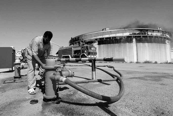 Un hombre conecta la manguera de un vehículo de bomberos a un hidrante cerca de un tanque de petróleo en una refinería de crudo, el
viernes, en la ciudad de Brega, Libia.  · Foto: Efe, Stringer