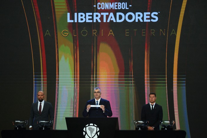 El director de Competiciones de Clubes de la Conmebol, Federico Nantes (c), junto al exfutbolista brasileño Felipe Melo (i) y el exfutbolista argentino Sebastián Battaglia, durante el sorteo de la fase de grupos de la Copa Libertadores, el 17 de marzo, en la sede de la Conmebol en Luque, Paraguay. · Foto: Daniel Duarte, AFP