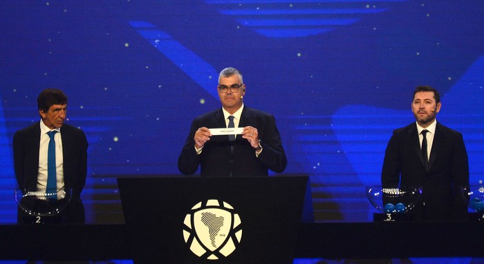 Frederico Nantes (c), director de Competiciones de Clubes de la Conmebol,  junto al entrenador de Racing, Gustavo Costas (i), y el futbolista chileno José Rojas, el 17 de marzo, en la sede de la Conmebol en Luque, Paraguay. · Foto: Daniel Duarte, AFP