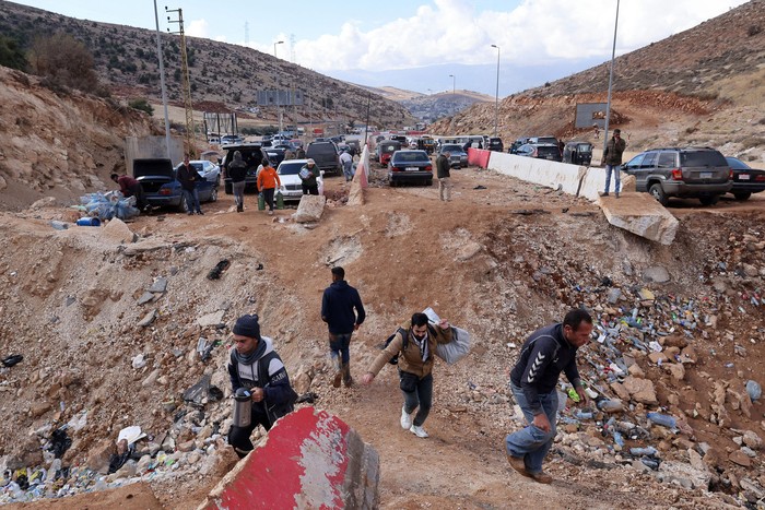 Personas que huyen de los bombardeos en Líbano cruzan un cráter causado por un ataque israelí, este miércoles, en el área de Masnaa, en el lado libanés del cruce fronterizo con Siria. · Foto: Anwar Amro, AFP.